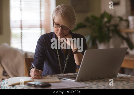Mature woman writing in diary while using laptop Stock Photo