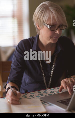 Mature woman using laptop while writing in diary Stock Photo
