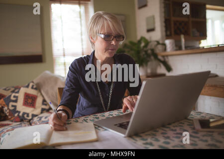 Mature woman using laptop while writing in diary Stock Photo