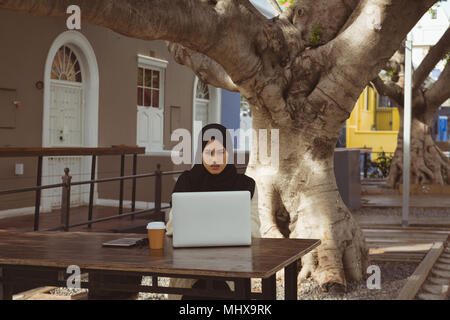Urban hijab woman using laptop at pavement cafe Stock Photo