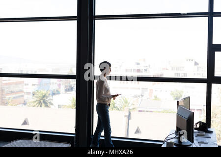 Mature businesswoman with mobile phone looking through window Stock Photo