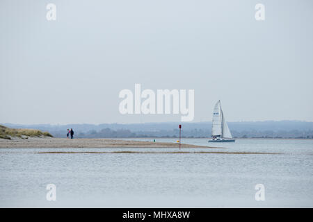 a young couple with their baby on the spit or Hoe at West Wittering with a yacht sailing in the background on a sunny cloudless day with the West down Stock Photo