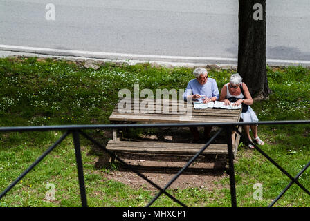 Old age tourists couple planning a trip on map while sitting on the park. Fiesole Florence, Italy Stock Photo