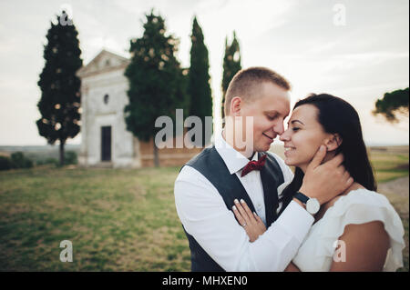 Happy stylish smiling couple walking and kissing in Tuscany, Italy on their wedding day. Stock Photo