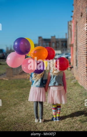 Two sisters holding hands with bunch of colourful balloons, rear view
