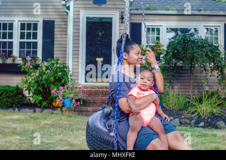 Mid adult woman on garden tire swing with baby daughter Stock Photo
