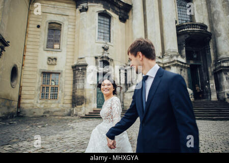 Elegant bride with groom walking near old catholic cathedral Stock Photo
