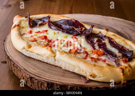 Turkish Pide with Pastirma , tomato and melted cheese on a wooden surface.