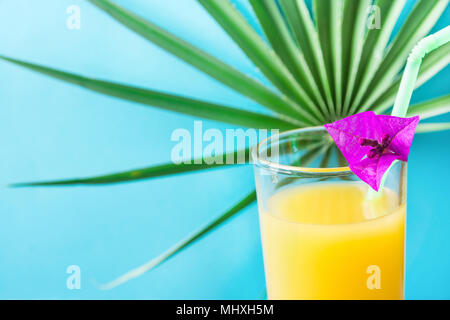 Close Up of Tall Glass with Freshly Pressed Tropical Fruits Juice Straw and Small Flower. Round Palm Tree Leaf on Blue Background. Vacation Summer Tra Stock Photo