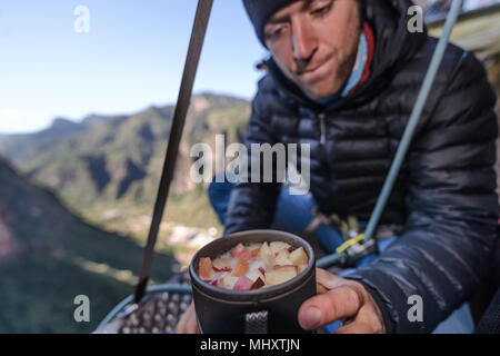 Rock climber on portaledge, preparing food, Liming, Yunnan Province, China Stock Photo