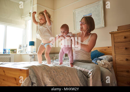 Woman on bed playing with baby and toddler daughters Stock Photo