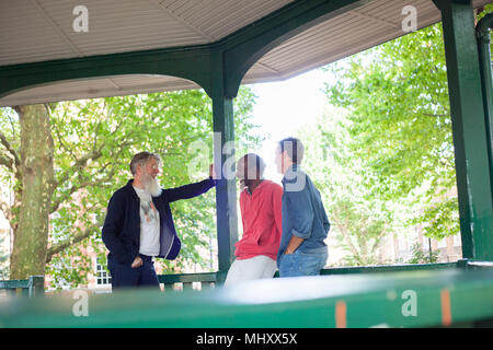 Three mature men, standing under bandstand, talking Stock Photo