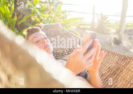Woman relaxing on hammock, using smartphone,  Nacpan Beach, Palawan, Philippines Stock Photo