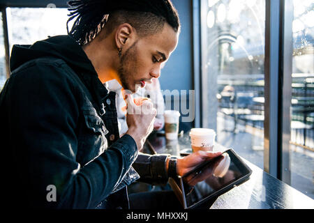 Young man sitting in coffee shop, looking at digital tablet, London, England, UK