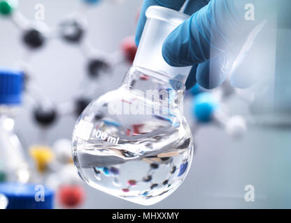 Scientist preparing chemical formula in a laboratory flask during an experiment, molecular model in the background
