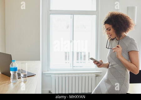 Businesswoman in office texting on smartphone Stock Photo
