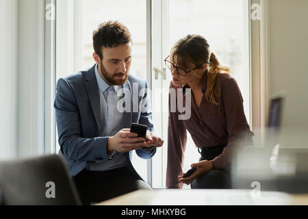 Colleagues in office looking at smartphone Stock Photo