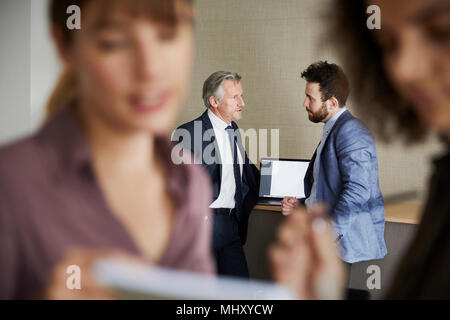 Colleagues in office chatting, focus on background Stock Photo