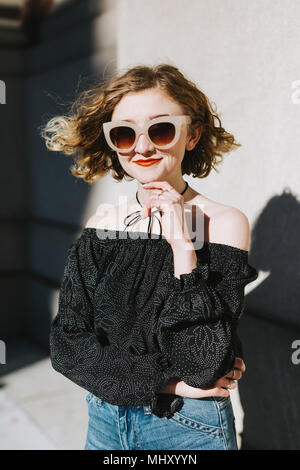 Portrait of red haired woman wearing sunglasses, looking at camera smiling Stock Photo