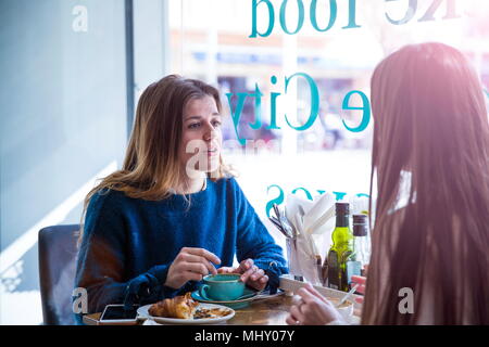 Two female friends sitting together in cafe, drinking coffee