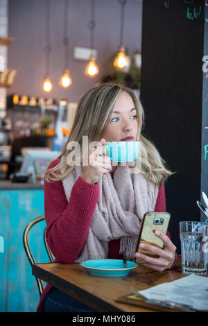Woman sitting in cafe, holding smartphone, drinking coffee Stock Photo