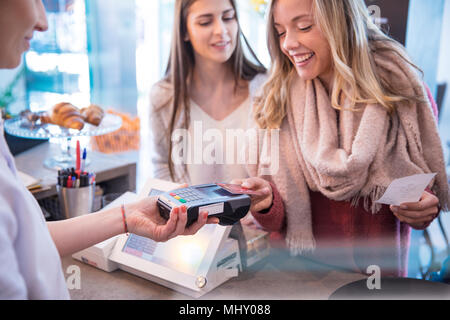 Female friends standing at counter in cafe, paying using credit card Stock Photo