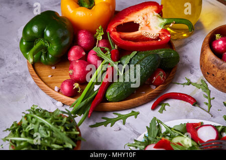 Creative fresh vegetable salad with ruccola, cucumber, tomatoes and raddish on white plate over textured background, close-up, selective focus. Mornin Stock Photo