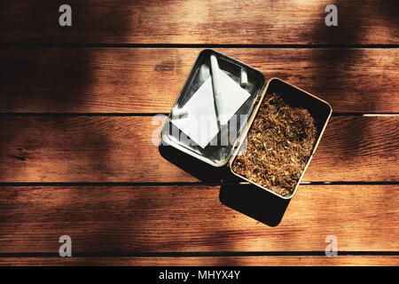 rolled cigarette, paper, filter and tobacco in a tin box on a wooden table background Stock Photo