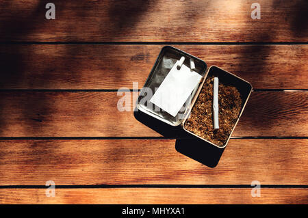 rolled cigarette, paper, filters and tobacco in a tin box on a wooden table background Stock Photo