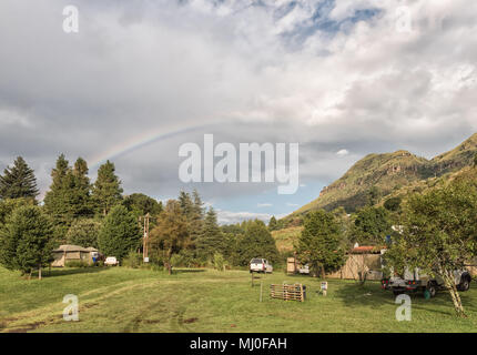 MONKS COWL, SOUTH AFRICA - MARCH 18, 2018: A rainbow over the camping site at Monks Cowl in the Kwazulu-Natal Drakensberg. A tent and vehicles are vis Stock Photo