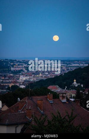 Evening view of Supermoon rising over old town. Night shot of Brno cityscape. Stock Photo