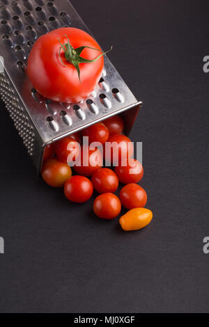 Culinary concept. Preparation recipe tomato juice. Large tomato and old grater down to small cherry tomatoes on dark background Stock Photo