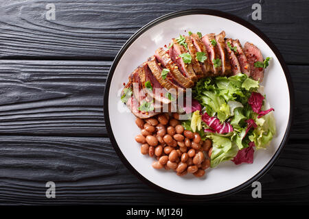 Serving grilled beef steak with fresh salad and beans close-up on a plate on a table. horizontal top view from above Stock Photo