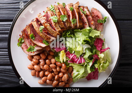 Grilled chopped beef steak with fresh salad and beans close-up on a plate. horizontal top view from above Stock Photo