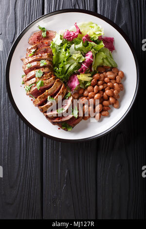 Serving grilled beef steak with fresh salad and beans close-up on a plate on a table. Vertical top view from above Stock Photo