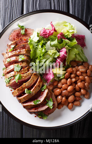 Grilled chopped beef steak with fresh salad and beans close-up on a plate. Vertical top view from above Stock Photo