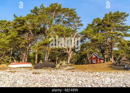 Boda coast eastern nature reserve on Oland, Sweden. Small red cabin among pine trees in the coastal forest. Boats upside down by the rocky beach. Love Stock Photo