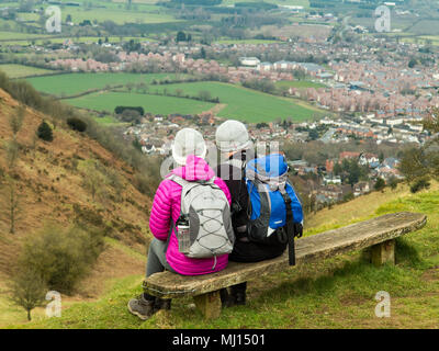 Man and woman couple sitting on a wooden bench on North Hill  above the town of Great Malvern Gloucestershire after walking along the Malvern Hills Stock Photo