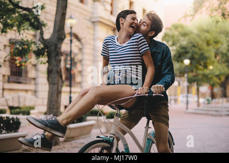 Laughing woman sitting on boyfriends bicycle handlebar. Cheerful couple on a bike together in the city having fun. Stock Photo