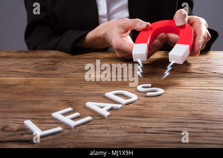 Businessperson Attracting White Lead Text With Horseshoe Magnet Over Wooden Desk Stock Photo