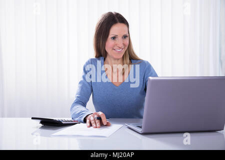Happy Mature Businesswoman Using Laptop At Workplace Stock Photo