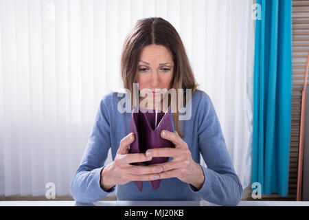 Close-up Of Unhappy Mature Woman Showing Her Empty Purse On Desk In Office Stock Photo