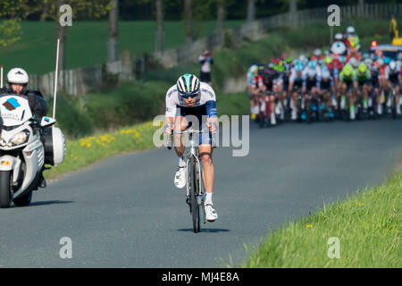 Denton, West Yorkshire, 4th May 2018. With strength & power, a single sunlit cyclist, has broken away from a large group of male cyclists in the pelaton, competing in the sunny Tour de Yorkshire 2018. They are racing past the grounds of Denton Hall, on a straight flat countryside lane near Ilkley, North Yorkshire, England, UK. Credit: Ian Lamond/Alamy Live News Stock Photo