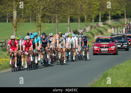 Denton, West Yorkshire, 4th May 2018. Large group of male cyclists in the pelaton, competing in the sunny Tour de Yorkshire 2018, are racing past the grounds of Denton Hall, on a straight, flat, scenic, countryside lane, closely followed by a line of team cars - near Ilkley, North Yorkshire, England, UK. Credit: Ian Lamond/Alamy Live News Stock Photo