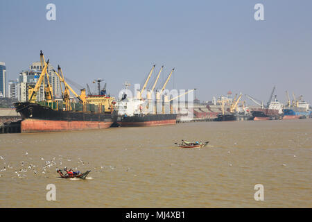 Cargo ships line the waterfront of the Yangon River port in Myanmar (Burma) with the Yangon city buildings in the background. Stock Photo