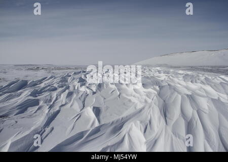 Beautiful patterns of sastrugi, parallel wavelike ridges caused by winds on surface of hard snow, with soft clouds in the sky, near Arviat Nunavut Stock Photo