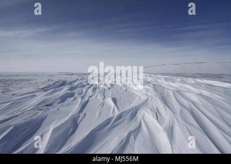 Beautiful patterns of sastrugi, parallel wavelike ridges caused by winds on surface of hard snow, with soft clouds in the sky, near Arviat Nunavut Stock Photo