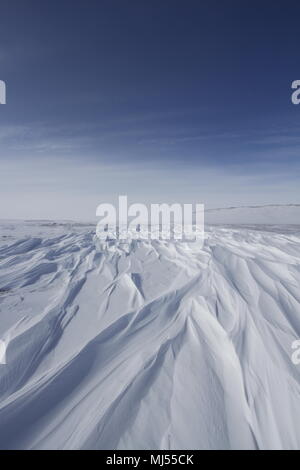 Beautiful patterns of sastrugi, parallel wavelike ridges caused by winds on surface of hard snow, with soft clouds in the sky, near Arviat Nunavut Stock Photo