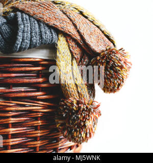 Stack of knitted winter scarfs on straw basket isolated on white background. Stock Photo