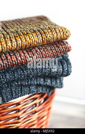 Stack of knitted winter scarfs on straw basket isolated on white background. Stock Photo